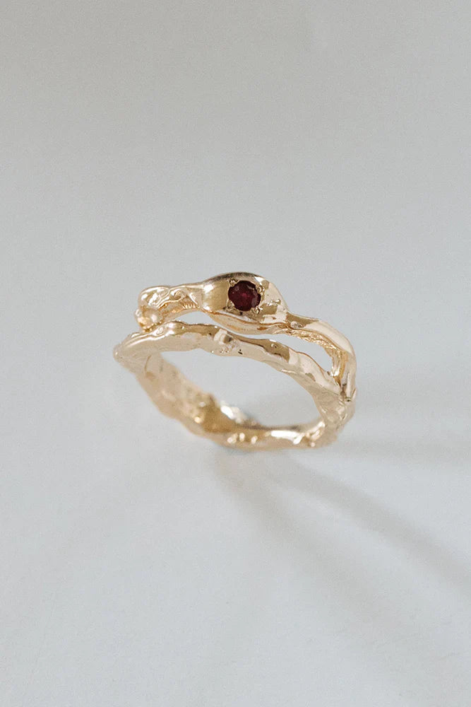 18ct yellow gold engagement ring featuring an organic, textured band design with a deep red gemstone accent, set against a neutral background.