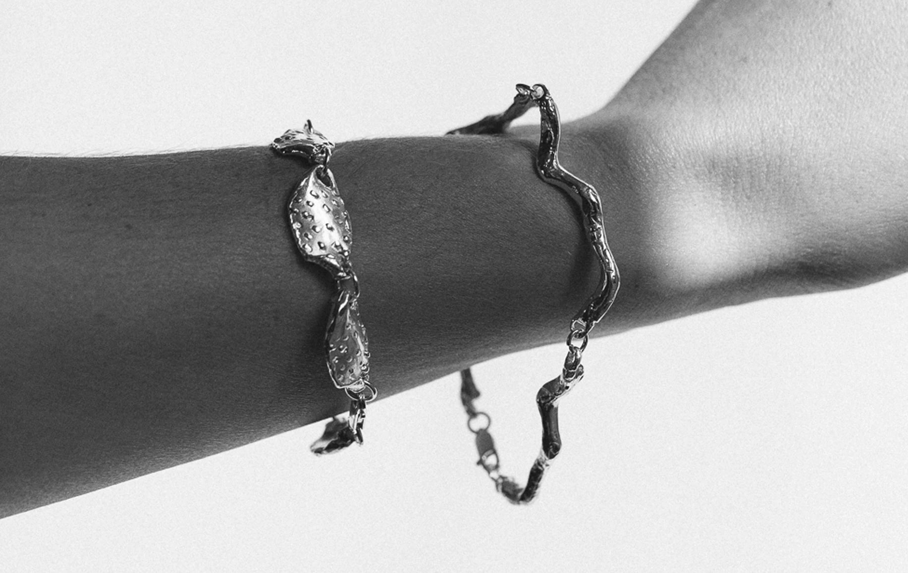 A gold chain bracelet with an organic, sculptural design, elegantly displayed on a raised hand against a clean white background.